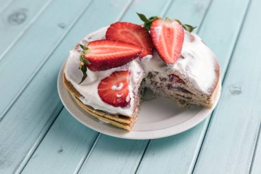 Çilekli krep pastası. Kremalı ve dutlu tatlı. Ulusal mutfak. Tahta masadaki tatlı hamur işleri. Turkuaz tahtaların arkaplanı.