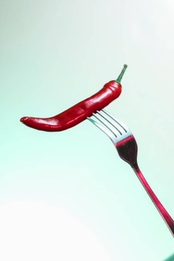 Red chili pepper on a fork. Sharp fork and about hot pepper. clipart
