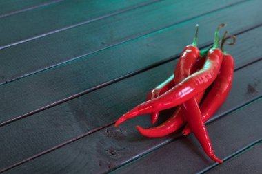 Koyu çıtçıtlardan yapılmış ahşap bir masada kırmızı biber. Siyah üzerine kırmızı. Popüler baharat. Zarif bir tat. Tahtaların tekrar eden çapraz çizgileri. Ateşli bir tadı var..