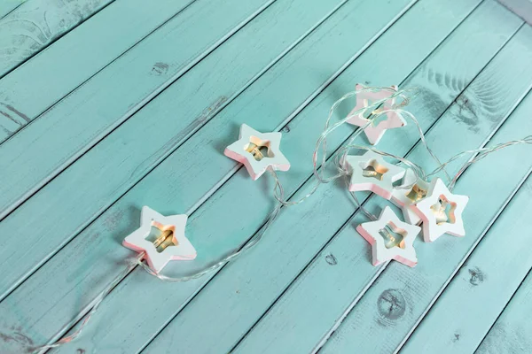 Garlands in the form of stars on an old mint-green rustic wooden background. Table made of turquoise boards.