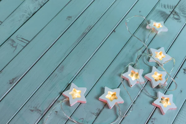 Garlands in the form of stars on an old mint-green rustic wooden background. Table made of turquoise boards.