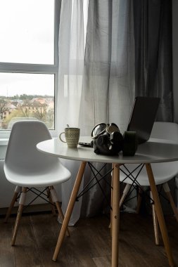 Müdürün iş yeri evde, karantina sırasında. Koronavirüs salgını sırasında iş. Laptop ve kahve. Kendini soyutlama sırasında çalış. Beyaz mutfak masası. Caddede büyük bir pencere var..