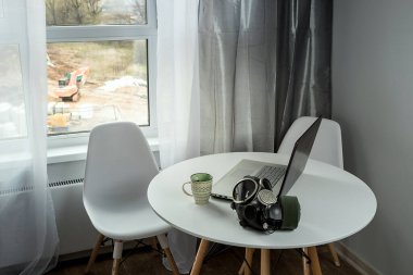 Müdürün iş yeri evde, karantina sırasında. Koronavirüs salgını sırasında iş. Laptop ve kahve. Kendini soyutlama sırasında çalış. Beyaz mutfak masası. Caddede büyük bir pencere var..