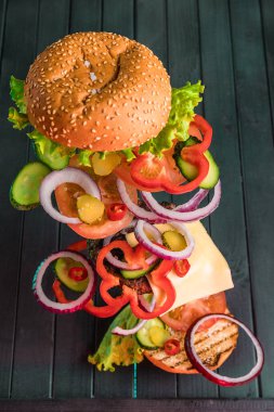 Sulu bir hamburgerin içeriği, arka planda karanlık bir zemine karşı havada yüzüyor. Hamburgerin bileşenleri havada donmuştu. İki rulo arasında sulu biftek ve taze sebze..