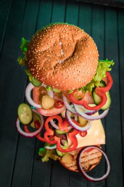 Sulu bir hamburgerin içeriği, arka planda karanlık bir zemine karşı havada yüzüyor. Hamburgerin bileşenleri havada donmuştu. İki rulo arasında sulu biftek ve taze sebze..