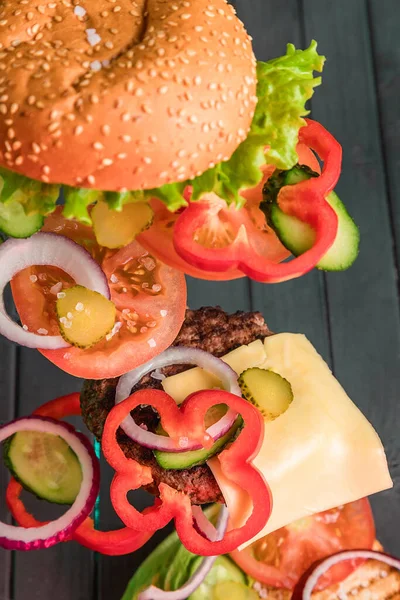 The ingredients of a juicy Burger float in the air, against a background of dark boards. The components of the Burger were frozen in the air. Juicy beef and fresh vegetables, between two rolls.