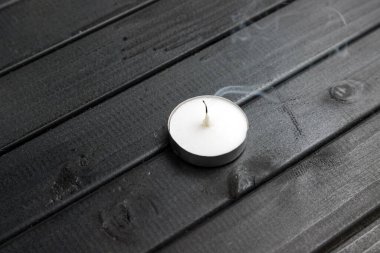 Koyu ahşap bir masada küçük beyaz bir mum. Sönmüş bir mumun dumanı. Siyah masa üstü tahtaları. dekoratif mum.