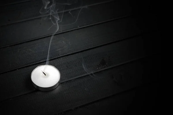 smoke from a extinguished candle. A small candle on a wooden table. Black boards. White on black.