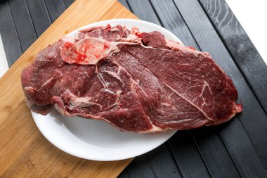 Beyaz tabakta bir parça taze et. Biftek. Et doğrama. Koyu bir masanın üzerindeki tahta kesme tahtası..