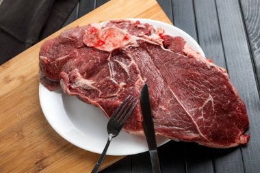 Beyaz tabakta bir parça taze et. Biftek. Et doğrama. Koyu bir masanın üzerindeki tahta kesme tahtası..