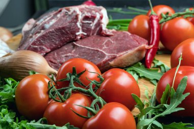 Taze et hazırlığı. Tahta bir masada taze biftek. Baharat ve sebzelerle çevrili et. Taze meyve. Kırmızı olgun domatesler. Beslenme yemeği..