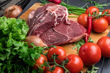 Taze et hazırlığı. Tahta bir masada taze biftek. Baharat ve sebzelerle çevrili et. Taze meyve. Kırmızı olgun domatesler. Beslenme yemeği..