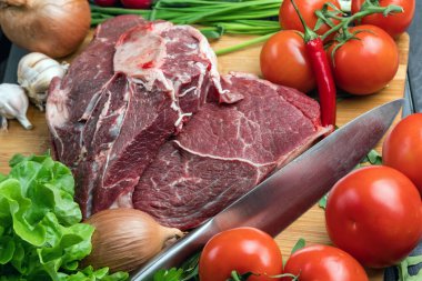 Taze et hazırlığı. Tahta bir masada taze biftek. Baharat ve sebzelerle çevrili et. Taze meyve. Kırmızı olgun domatesler. Beslenme yemeği..