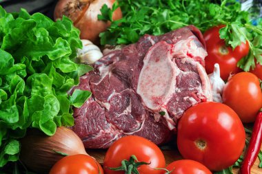 Taze et hazırlığı. Tahta bir masada taze biftek. Baharat ve sebzelerle çevrili et. Taze meyve. Kırmızı olgun domatesler. Beslenme yemeği..