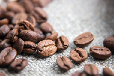 Kahverengi kahve çekirdekleri yakın plan. Tahıllar güzel bir dokuya sahip bir çuvalın üzerinde yatıyor. Kahvenin makrofotoğrafçılığı. Güzel taneler.