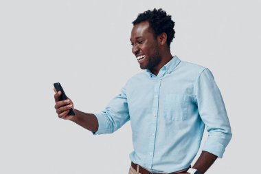 Gri arka planda dururken video konferansı kullanarak konuşan yakışıklı bir Afrikalı.