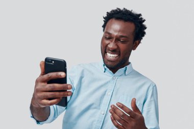 Yakışıklı Afrikalı genç adam, gri arka planda dikilirken video konferans kullanarak konuşuyor ve gülümsüyor.