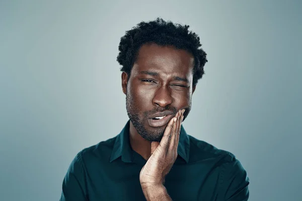 Frustrated young African man making a face while standing against grey background