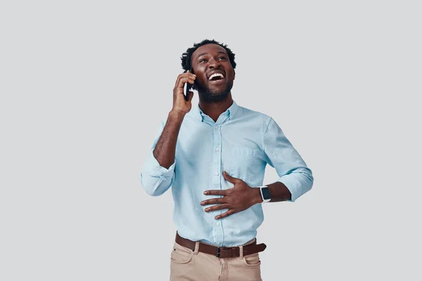 Beau jeune homme africain parlant au téléphone et souriant tout en se tenant debout sur fond gris — Photo