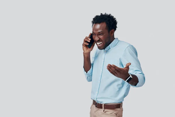 Όμορφος νεαρός Αφρικανός μιλάει στο τηλέφωνο και χαμογελάει ενώ στέκεται στο γκρίζο φόντο — Φωτογραφία Αρχείου