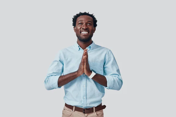 Όμορφος νεαρός Αφρικανός που κρατάει τα χέρια του σφιγμένα και χαμογελαστά ενώ στέκεται στο γκρίζο φόντο — Φωτογραφία Αρχείου