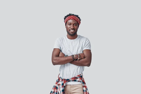 Όμορφος νεαρός Αφρικανός κοιτάζει την κάμερα και χαμογελά ενώ στέκεται στο γκρίζο φόντο — Φωτογραφία Αρχείου