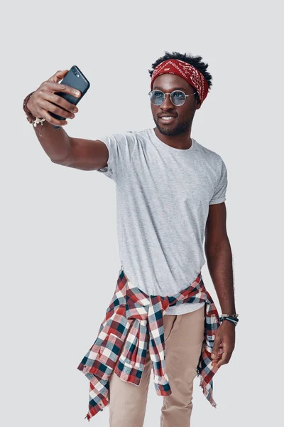 Όμορφος νεαρός Αφρικανός βγάζει σέλφι και χαμογελάει ενώ στέκεται στο γκρίζο φόντο — Φωτογραφία Αρχείου