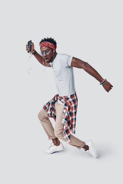 Volledige lengte van knappe jonge Afrikaanse man dansen en het maken van een gezicht terwijl staan tegen grijze achtergrond — Stockfoto