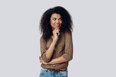 Çekici genç Afrikalı kadın, gri arka planda dururken gülümsüyor ve başka tarafa bakıyor.