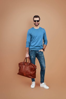 Kahverengi arka planda dikilirken gülümseyen ve kameraya bakan zarif bir genç.              