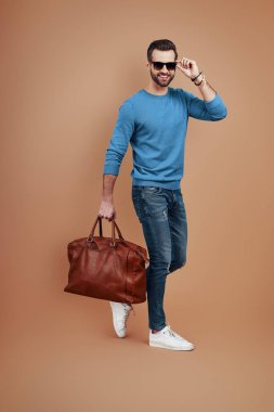 Kahverengi arka planda yürürken gülümseyen ve kameraya bakan yakışıklı bir genç.           