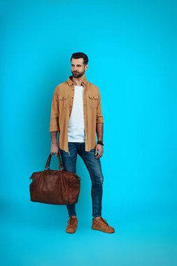 Mavi arka planda dikilirken gülümseyen ve yüzünü çeviren zarif genç adam.            