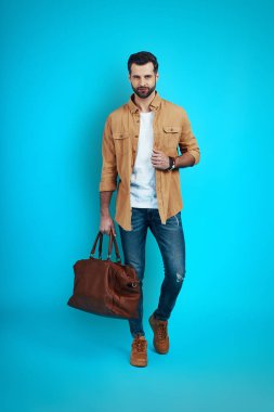 Mavi arka planda yürürken kameraya bakıp gülümseyen yakışıklı bir genç.             