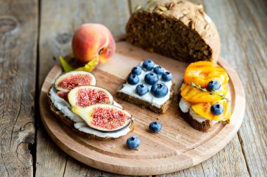Tahtada ev yapımı ekmek. Böğürtlen, incir ve peynirli şeftali. Vejetaryen yemeği. Düzgün beslenme. Atıştırmalık Tahtada dilimlenmiş ekmek.