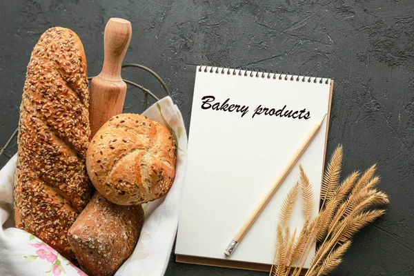 Bread in a basket on a black background. Assorted baking in a metal basket. Place for recipe and text. Background with rolling pin and flour. Rye bread and baguette with seeds. Buckwheat bread