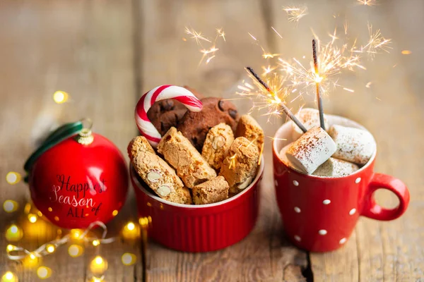 Christmas cookies on a wooden table with cocoa and marshmallows. Christmas candy with a toy on the Christmas tree. Hot Christmas drink with chocolate chip cookies. Sparkler in a cup. Christmas 2020