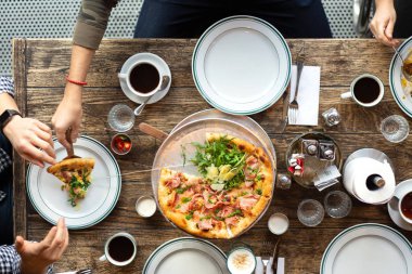 Masadaki arkadaşlar pizza yer. Şirket bir restoranda toplandı. Öğle yemeği, işte atıştırmalık bir şeyler. Pizza partisi. İnsanlar pizza dilimleri alıyor. Masa ayarı. İnsanlar fast food yiyor. Masada kahve var..