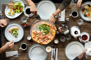 Masadaki arkadaşlar pizza yer. Şirket bir restoranda toplandı. Öğle yemeği, işte atıştırmalık bir şeyler. Pizza partisi. İnsanlar pizza dilimleri alıyor. Masa ayarı. İnsanlar fast food yiyor. Masada kahve var..