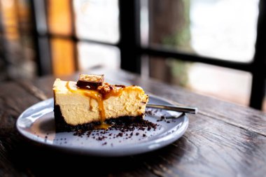 Tahta bir masanın üzerinde bir fincan kahveyle bir dilim cheesecake. Ceviz ve karamel ile cheesecake. Snickers peynirli keki. Karamelli turta. Patlamış mısırlı karamel peynirli kek. Bardakta latte ile tatlı.