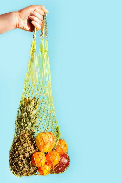 Mesh bag with fruit in the hands. Modern reusable stores, zero waste concept.Bag for laceMesh bag with fresh tangerines, pineapple and apples. Healthy tropical fruit. Food retail.