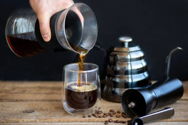 Hot coffee is pouring into a glass. Brewing coffee through a funnel. A cup of fresh hot filter. A grinder with a teapot and coffee grains. Fragrant hot drink. Home-brewing coffee. Coffee break