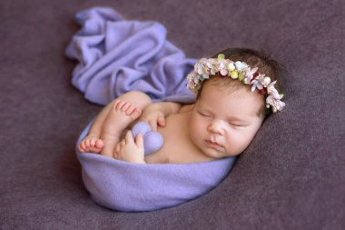 Kafasında çelenk olan yeni doğmuş bir bebek. Bahar. Bahar kompozisyonu. Yeni doğanların fotoşopu. Güzel kız. Ellerinde bir kalple yeni doğmuş bir bebek.