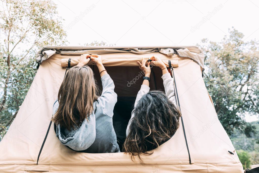 Two young girls friends secure the tent before staying overnight in the wild