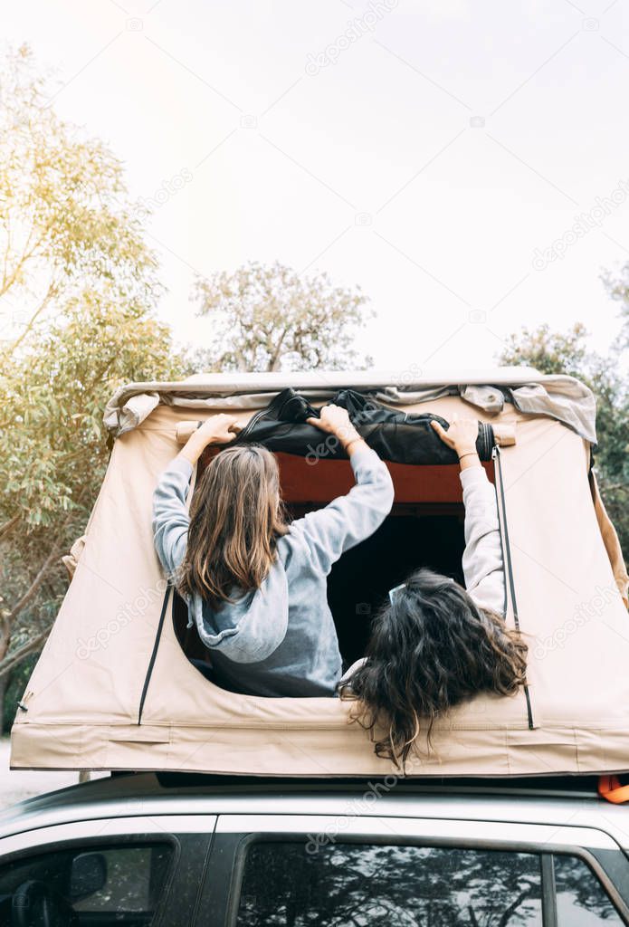 Two happy friends set up a rooftop tent over the car