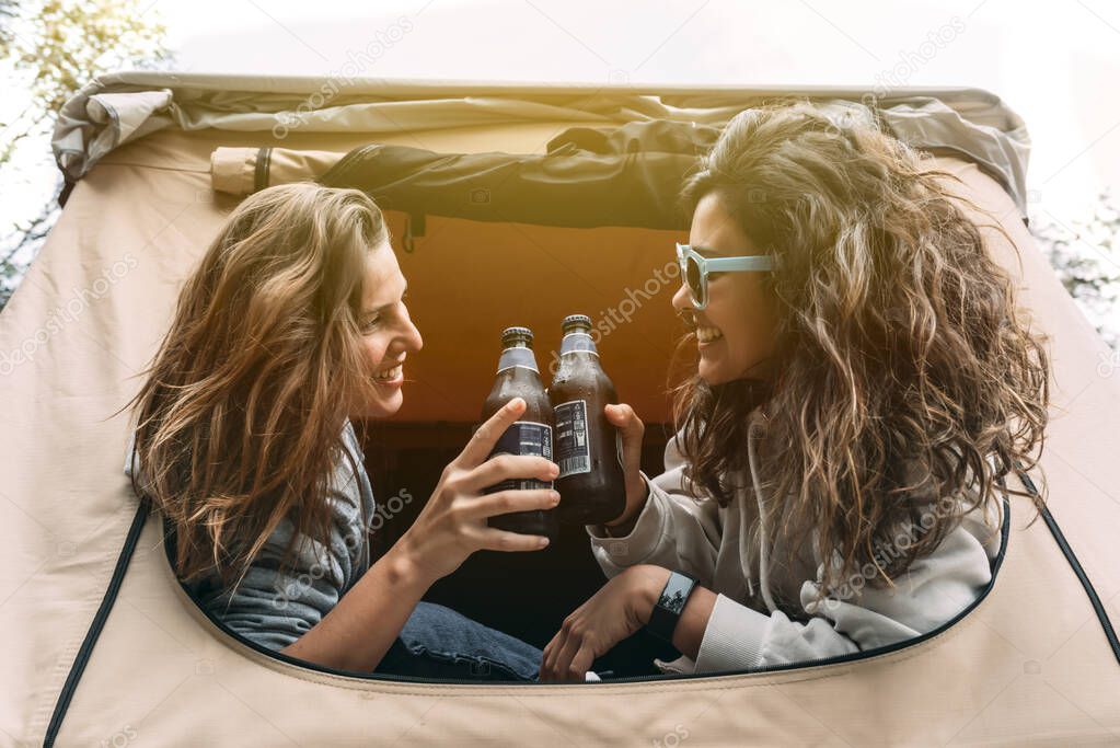 Two lovely camper girls drink beers in their rooftop tent