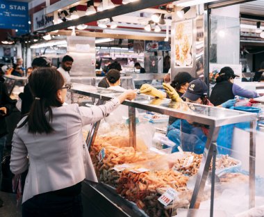 Melbourne, Avustralya; Mart 2020. Bir kadın Melbourne, Footscray Market 'te bir marketten balık alıyor. Süpermarketler ve market çalışanları Coronavirüs nedeniyle eldiven ve maske kullanırlar. Gıda fiyatı artıyor.