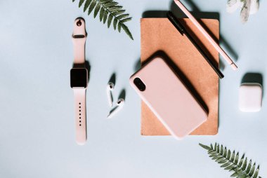 Modern bir akıllı telefonu, akıllı saati, kablosuz kulaklığı, not defteri ve kalemi olan güzel bir ev ofisi. Pembe ve mavi renkler. Yazılacak metin boşluğu. Üretkenliği arttırmak için minimalist stil