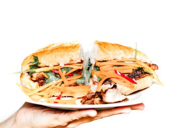 Sebzeli ve domuz rostolu geleneksel Vietnam sandviçi olan Banh mi servis eden bir insan eli. Telif uzayı olan beyaz arkaplan. Fransız etkisi Vietnam mutfağında baget ekmeği yüzünden. Sokak yemeği..