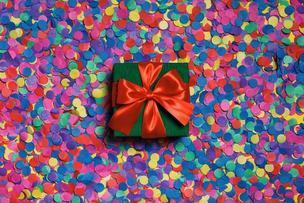 Caja verde con un regalo y una cinta roja en confeti disperso —  Fotos de Stock
