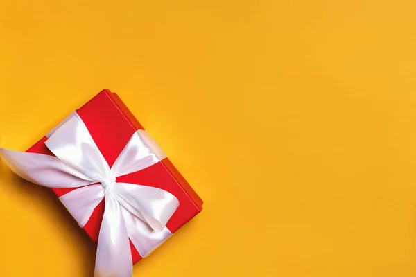 Primo piano di una scatola rossa con un regalo e un nastro bianco su uno sfondo giallo — Foto Stock